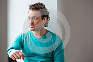 Handsome pensive young man sitting and looking at the window