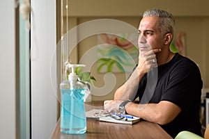 Handsome Persian man with gray hair thinking by window at the library