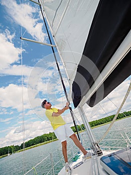 Handsome person raise the sail on a sailing yacht, summer vacations on sailboat