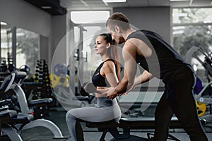 Handsome personal instructor helping his female client to training with dumbbells.