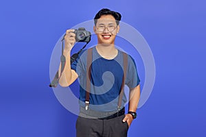 Handsome photographer showing professional camera and smiling cheerfully on purple background