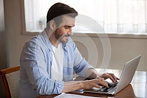 Handsome pleasant young man working remotely on computer at home.