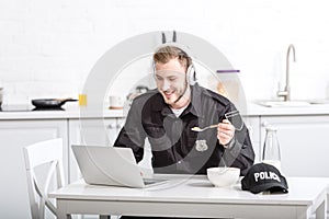 Handsome police officer eating cornflakes and using laptop