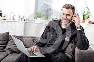 Handsome policeman sitting on sofa with laptop and listening