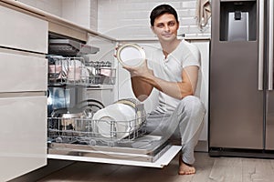 handsome positive man putting plates in dishwasher machine