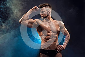 Handsome power athletic man bodybuilder. Wet Fitness muscular body on dark smoke background.