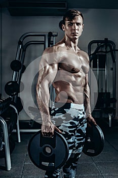 Handsome power athletic man on diet training pumping up muscles with dumbbell and barbell. Strong bodybuilder, perfect