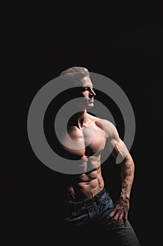 Handsome power athletic man in dramatic light. Strong bodybuilder with perfect shoulders, biceps, triceps, back, delta