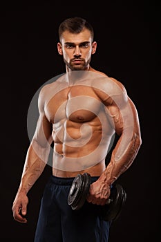 Handsome power athletic man with dumbbell is confidently looking forward. Strong bodybuilder with six pack, perfect abs