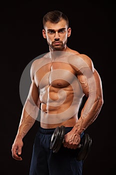 Handsome power athletic man with dumbbell is confidently looking forward. Strong bodybuilder with six pack, perfect abs