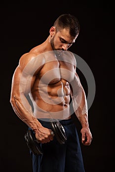 Handsome power athletic man with dumbbell is confidently looking forward. Strong bodybuilder with six pack, perfect abs