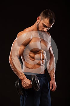 Handsome power athletic man with dumbbell is confidently looking forward. Strong bodybuilder with six pack, perfect abs