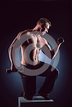 Handsome power athletic man in training pumping up muscles with dumbbells. Fitness muscular bodybuilder lifting dumbbell
