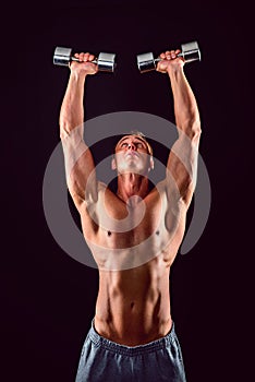 Handsome power athletic man in training pumping up muscles with dumbbells. Fitness muscular bodybuilder lifting dumbbell