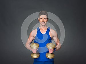 Handsome power athletic man in training pumping up muscles with dumbbells in a gym.