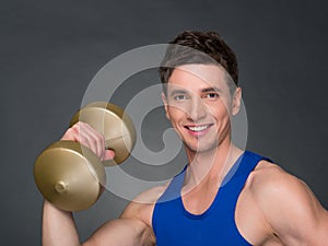 Handsome power athletic man in training pumping up muscles with dumbbells in a gym.