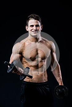 Handsome power athletic man training pumping up muscles with dumbbells in a gym. Fitness muscular body on black