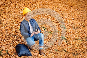 Handsome preteen boy using smartphone on a walk in autumn park. Stylish schoolboy walking after school. People, technology,