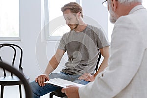 Handsome problematic patient during counseling with grey senior therapist