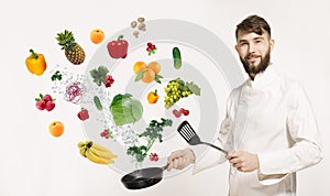 Handsome professional chef in uniform uggling with vegetables and other food in the kitchen. Chef and flying vegetables and fruits