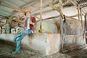 handsome rancher wearing a cowboy hat poses sitting with one thumbs up while using a digital tablet