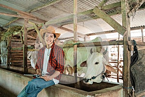 handsome rancher wearing a cowboy hat sitting in a cage holding a digital tablet