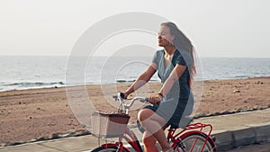Handsome red hair female in green dress ride vintage bicycle along coast line