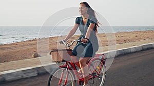 Handsome red hair female in green dress ride vintage bicycle along coast line