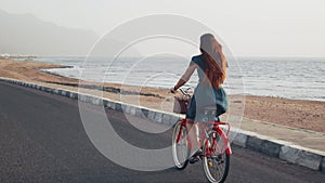 Handsome red hair female in green dress ride vintage bicycle along coast line