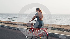 Handsome red hair female in green dress ride vintage bicycle along coast line