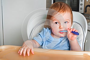 Handsome red-haired baby eating in children`s chair. First feeding children with porridge, vegetables, fruits, meat