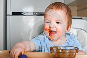 Handsome red-haired baby eating in children`s chair. First feeding children with porridge, vegetables, fruits, meat