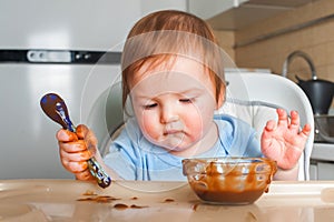 Handsome red-haired baby eating in children`s chair. First feeding children with porridge, vegetables, fruits, meat