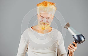 Handsome redhead man with long hair dries his hair with a hairdryer. Blonde bearded man with hair dryer.