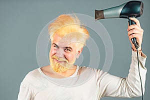 Handsome redhead man with long hair dries his hair with a hairdryer. Blonde man with hair dryer.