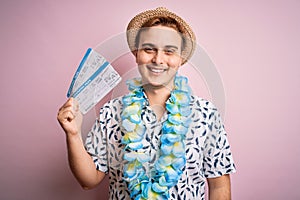 Handsome redhead tourist man on vacation wearing hawaiian lei holding boarding pass airlane looking positive and happy standing