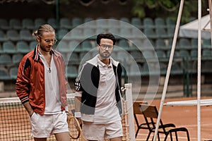 handsome retro styled tennis players walking with rackets at tennis court