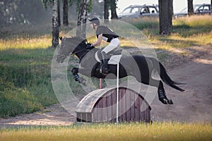 Handsome rider man jumping over obstacle on black stallion horse during eventing cross country competition