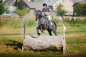 Handsome rider man jumping over obstacle on black stallion horse during eventing cross country competition