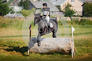 Handsome rider man jumping over obstacle on black stallion horse during eventing cross country competition