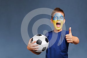 Handsome screaming Ukrainian fanboy holds soccer ball and gesturing thumbs up