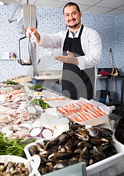 Handsome seller in black apron showing fish photo