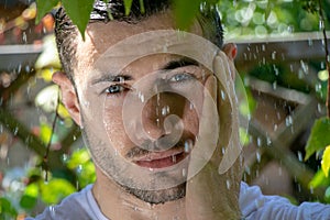 Handsome semi naked man with muscles and bare chest caught in shower of rain in garden