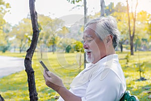 Handsome senior asian man chatting with his family on video call of smart phone by using internet online service at park or Elderl