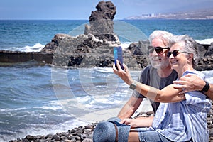 Handsome senior couple sitting on the rocks smiling taking a selfie. Two retired enjoying summer vacation and freedom