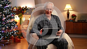 Handsome senior grey-haired man in rocking chair waving talking at digital tablet web chat smiling. Portrait of