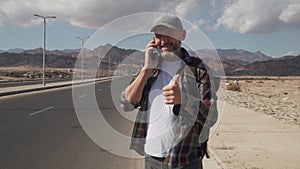 Handsome senior male talking by smatrphone standing on a road in desert