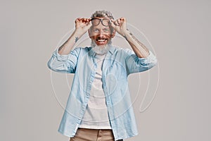 Handsome senior man adjusting eyewear and smiling while standing against gray background