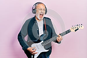 Handsome senior man with beard playing electric guitar angry and mad screaming frustrated and furious, shouting with anger