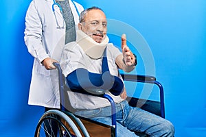 Handsome senior man with beard sitting on wheelchair with neck collar smiling friendly offering handshake as greeting and